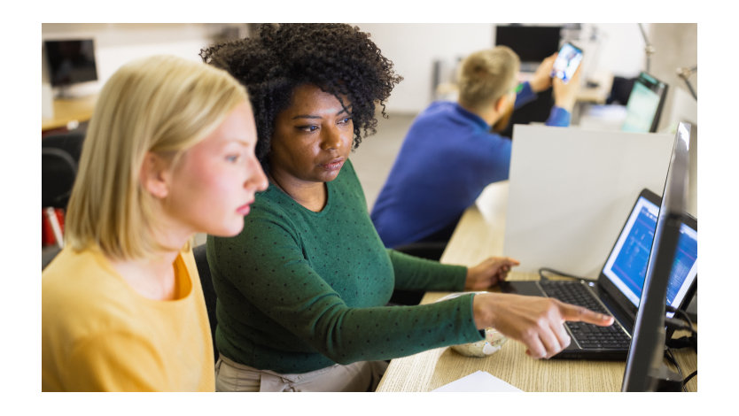 Student in a classroom directs another student’s attention to a computer monitor.