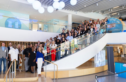 A diverse group of Microsoft TechSpark fellows fill a long stairway in a corporate office are posed for a group photo.