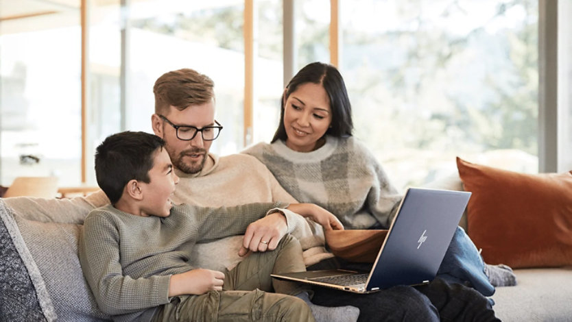 A family sitting on a couch and looking at a laptop together.