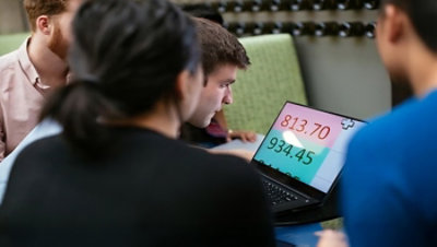 Four young adults look at an enlarged Excel spreadsheet on a laptop.