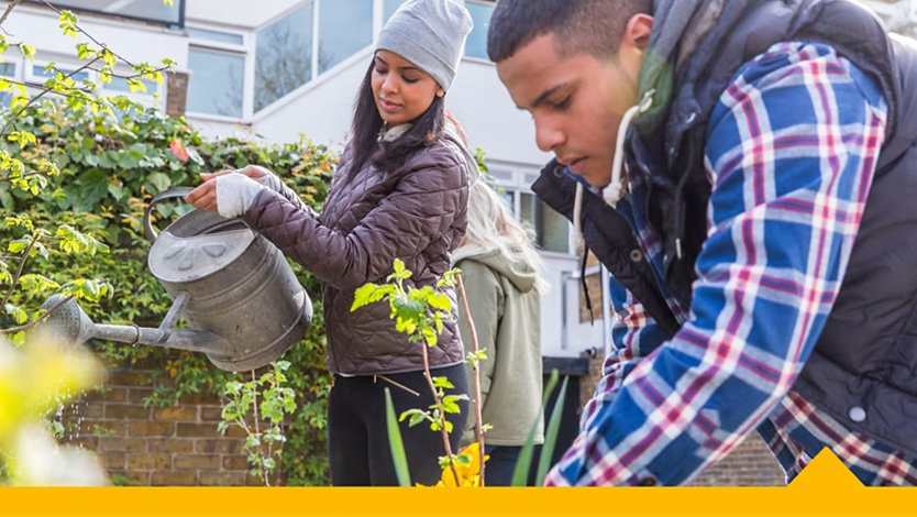 Two volunteers tend to a flower bed outside a corporate office.
