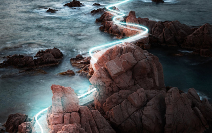A glowing light trail winds across rocks in the ocean.