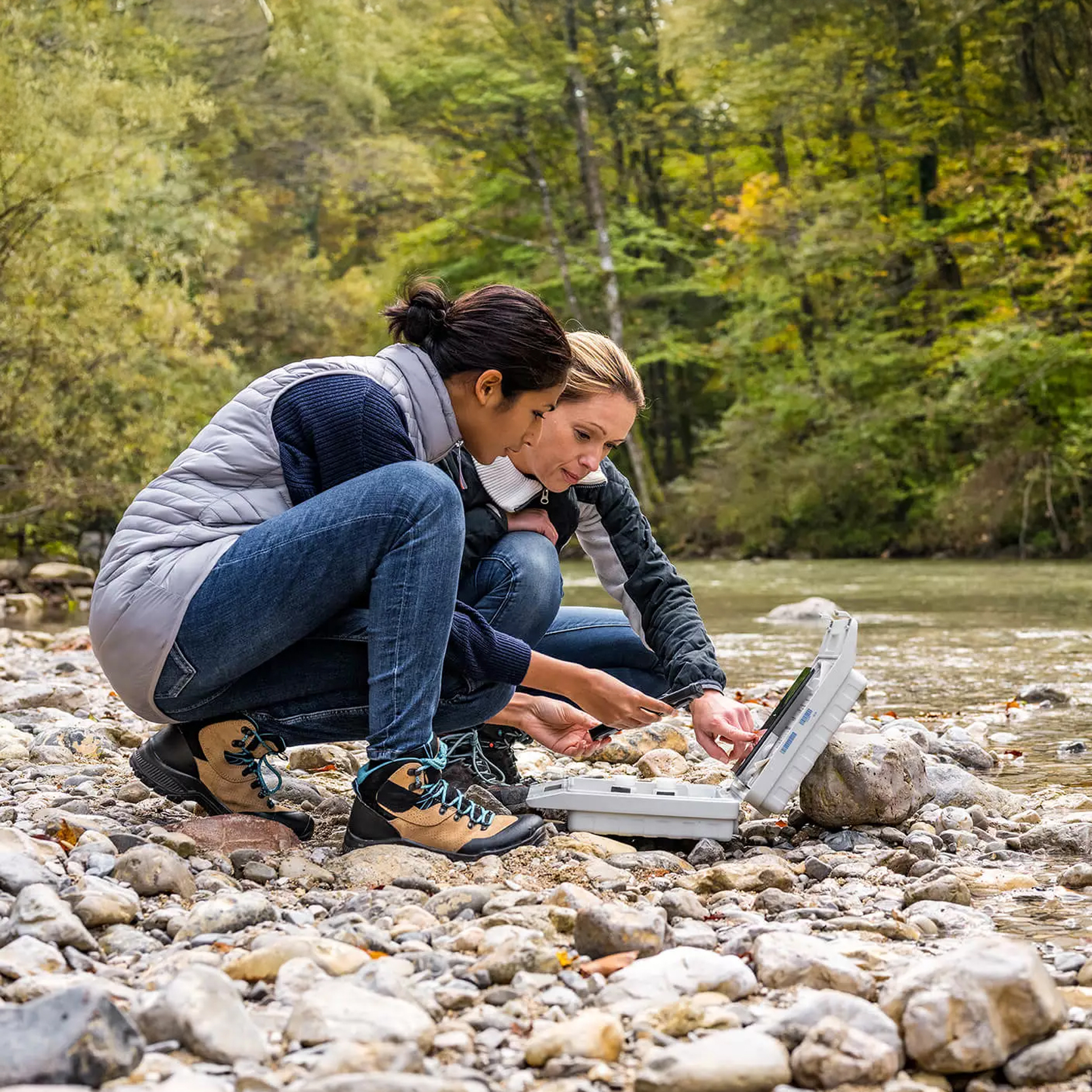 Natural river water samples are collected and tested by two women while a forest serves as the background.