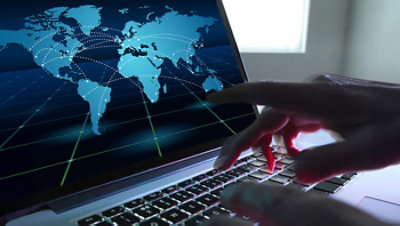 A world map with connected nodes is displayed on a laptop screen as a person types.