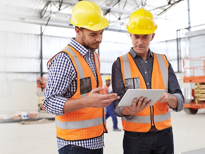 Two construction workers looking at a tablet.