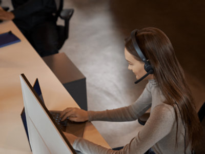Seorang perempuan mengenakan headset bekerja menggunakan laptop.
