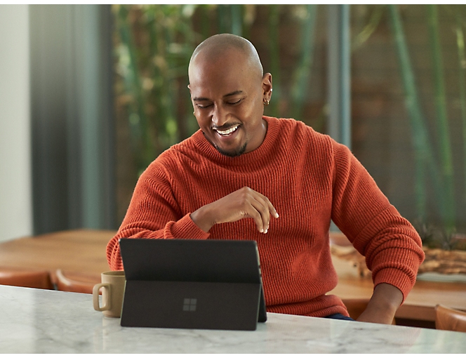 テーブルに座って Microsoft Surface Laptop を使用している女性。