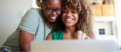 Dve ženski se smejita in objemata med gledanjem na prenosnik v svetli, domači sobi.