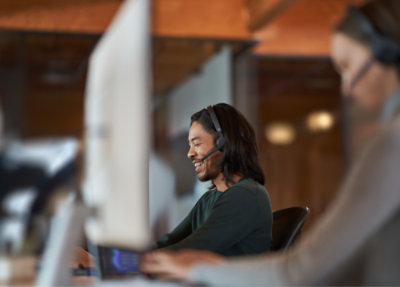 Uśmiechnięty przedstawiciel obsługi klienta w zestawie słuchawkowym pracujący na komputerze.