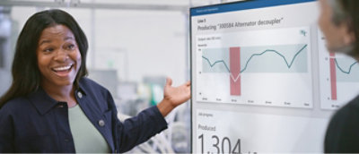 A woman smiling and a pointing to a screen showing some statistics