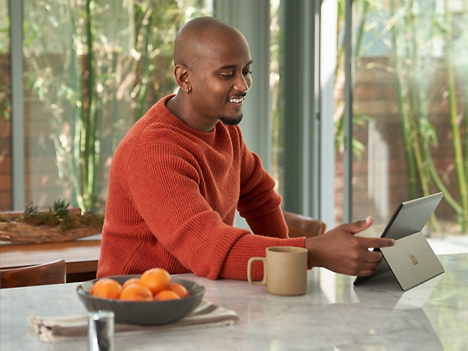 Uma pessoa usando um tablet e sorrindo com café e frutas sobre a mesa