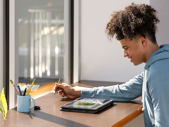 Siedząca w biurze osoba korzystająca z tabletu za pomocą pióra cyfrowego z umieszczonym na stole stojakiem na pióro