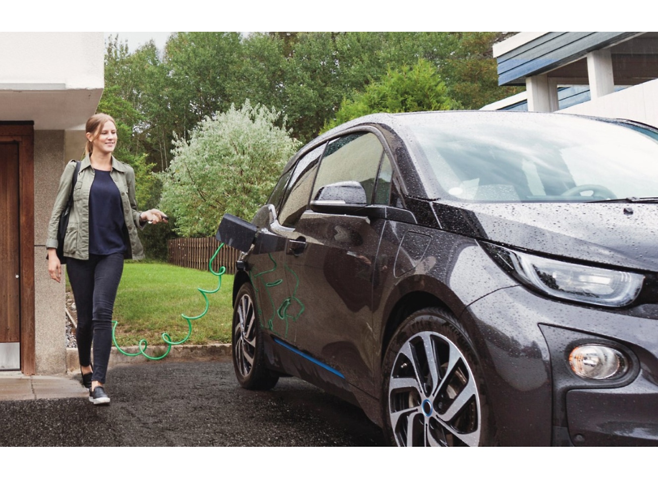 A woman is charging her BMW i3 in front of a house.