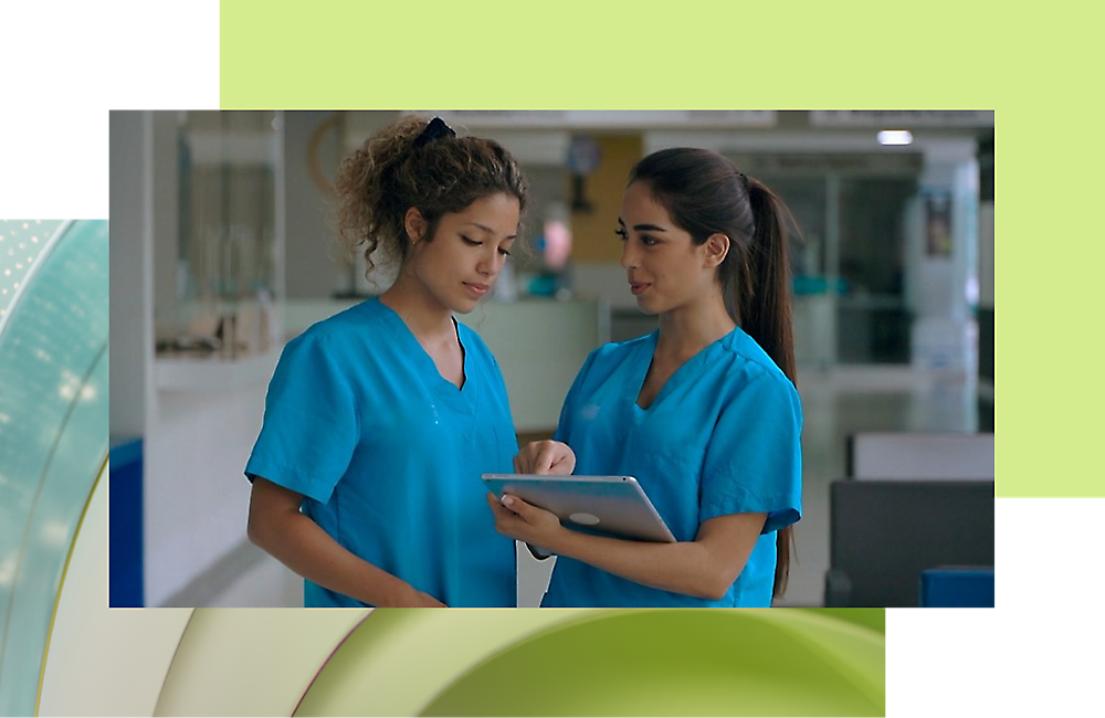 A pair of women wearing blue scrubs and having a discussion while one person holding a tablet.