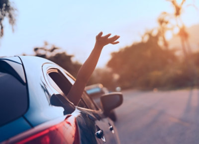 Véhicule roulant sur une route au coucher du soleil avec une main tendue par la fenêtre