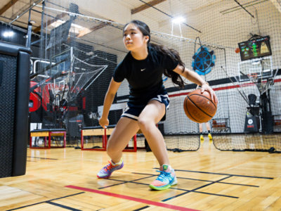 Young girl dribbles a basketball on an indoor court.