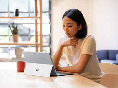 テーブルに座り、Surface Pro 13インチ用フレックスキーボードを接続した「Surface Pro for Business」で作業している人。