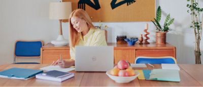 A person sitting at a table with a computer and a bowl of fruit