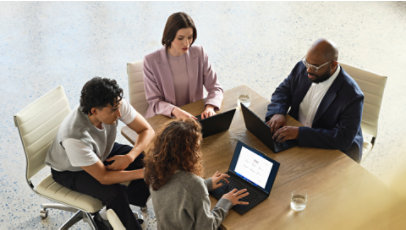 Professionals gather around a table and look at a laptop during a meeting.