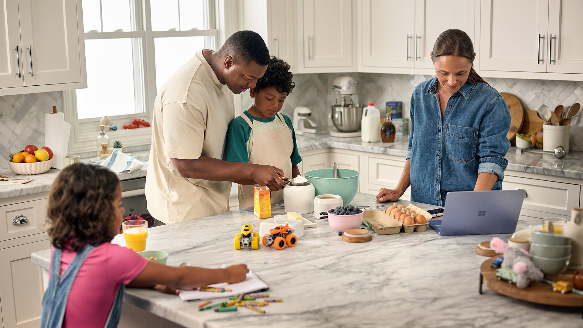 A family of four cook together in a kitchen while the mother reads a recipe from her Surface Laptop. 