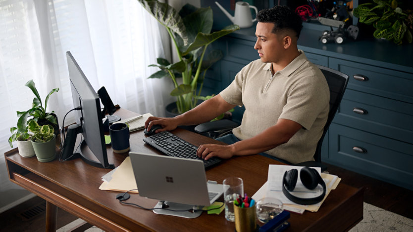 Un homme assis à un bureau, en train de travailler sur un Surface Laptop et un moniteur externe. 