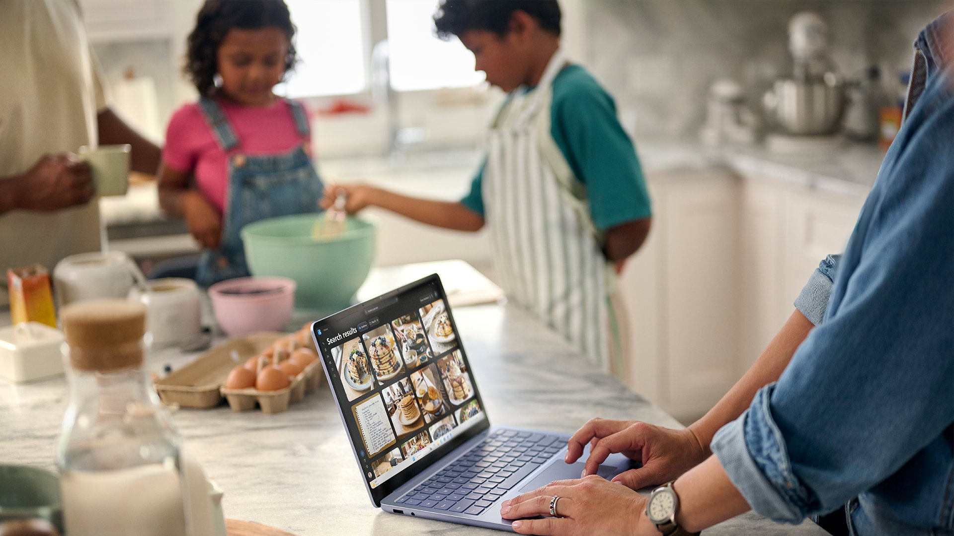 A family cooks together in a kitchen with a recipe pulled up on the screen of a Surface Laptop. 