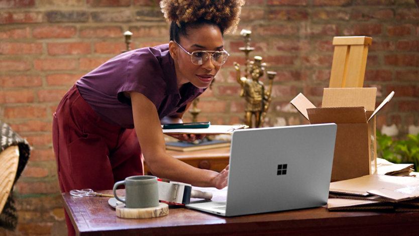 Une femme travaille sur un Surface Laptop dans une salle ensoleillée remplie de plantes. 