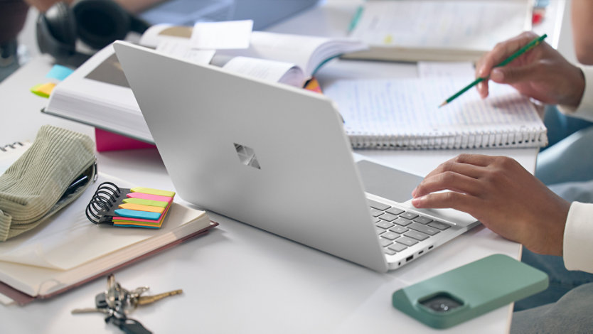 Bir kütüphane masasında, çeşitli çalışma materyallerinin arasında duran Surface Laptop.
