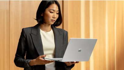 A business professional holds an open Surface laptop in front of light curtains.
