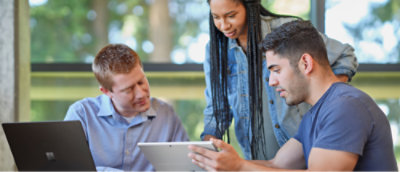 Three colleagues discussing over digital tablets in a brightly lit office space.
