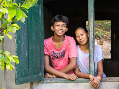 An adolescent boy and a middle aged woman standing together, looking out an open window.