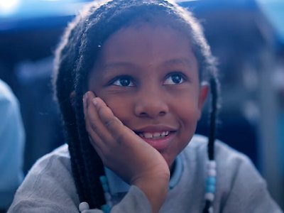 A young Black girl listens raptly to her teacher. 