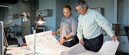 Two people looking at blueprints in an office.
