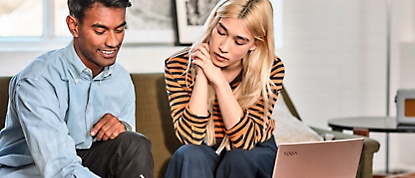 A man and woman sitting on a couch looking at a laptop.