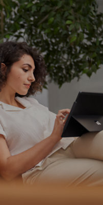 Жінка сидить на дивані й працює на пристрої Surface Pro