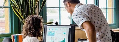 Zwei Personen, die auf einen Desktopmonitor schauen, auf dem ein Dashboard mit Grafiken und Diagramme angezeigt wird 