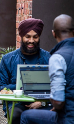 Twee personen die buiten zitten en werken met de laptops op de tafel