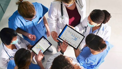 一群医疗保健专业人员挤在两台平板电脑周围,上面显示了患者信息.