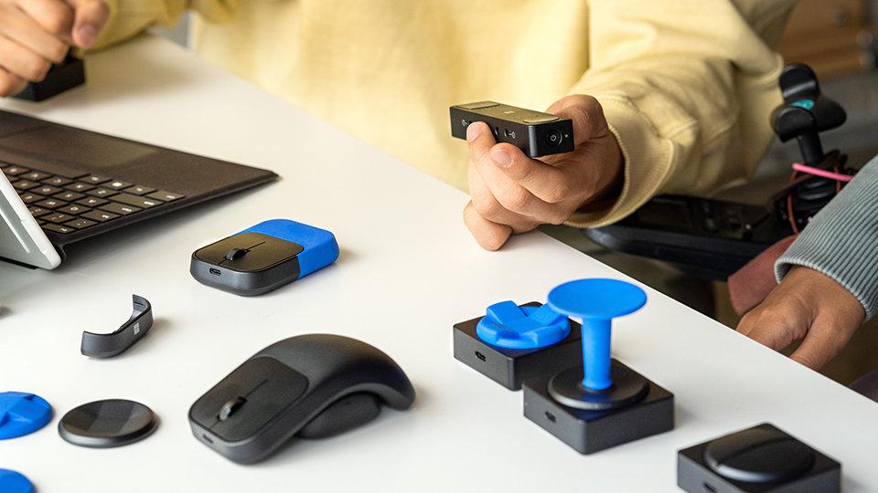 Une personne en fauteuil roulant met en place Hub adaptatif de Microsoft et Buttons avec des accessoires imprimés en 3D.