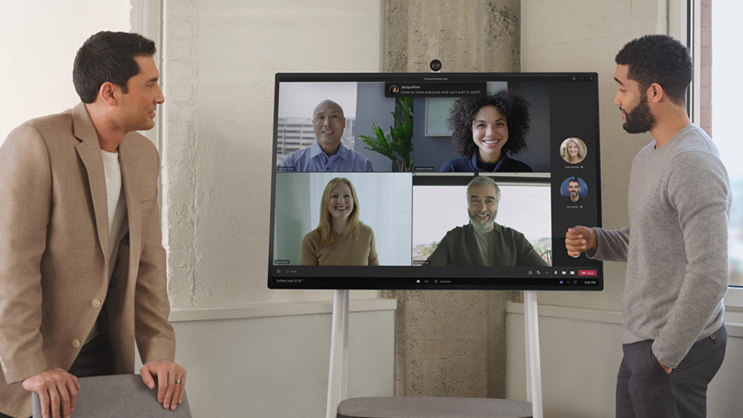 Two coworkers interact with remote team members via a Teams call on a Surface Hub 2S
