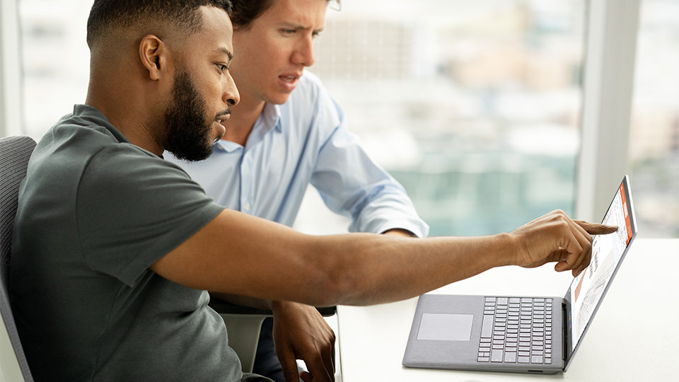 Dos compañeros de trabajo revisan tu trabajo de forma segura en Surface Laptop 5 para empresas.