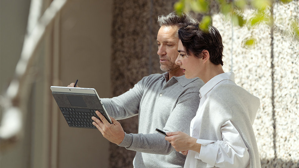 Twee collega's bekijken informatie op Surface Pro 9 voor zakelijk gebruik terwijl ze op locatie werken.