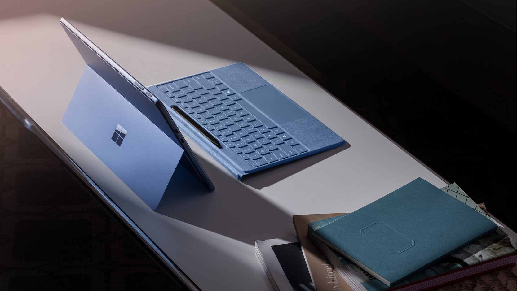 Um Teclado Flex para Surface Pro com Slim Pen destacado de um dispositivo Surface sobre uma mesa com outros itens diversos.
