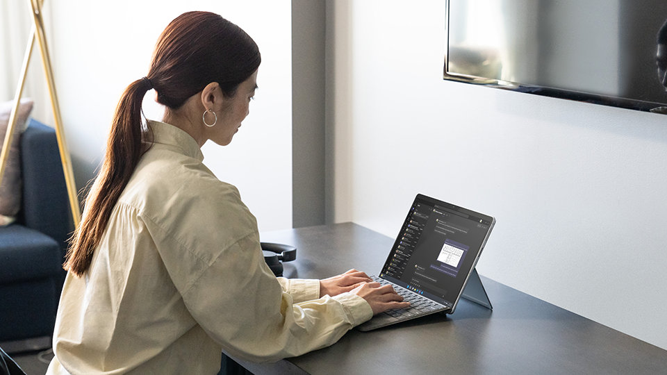 A person uses a Surface Pro Signature Keyboard for Business while seated at a desk.