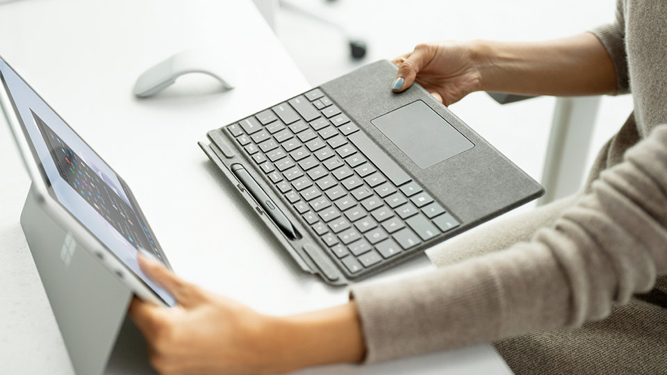 Eine Person bringt ein Surface Pro Signature Keyboard an einem Surface Pro 9 an.