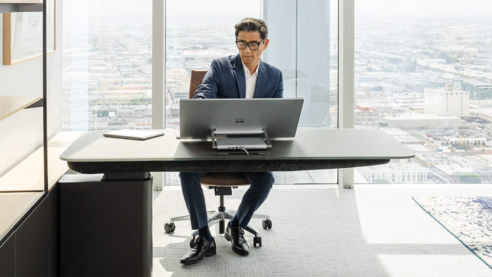 A person sits at a desk, working on Surface Studio 2+ for Business.