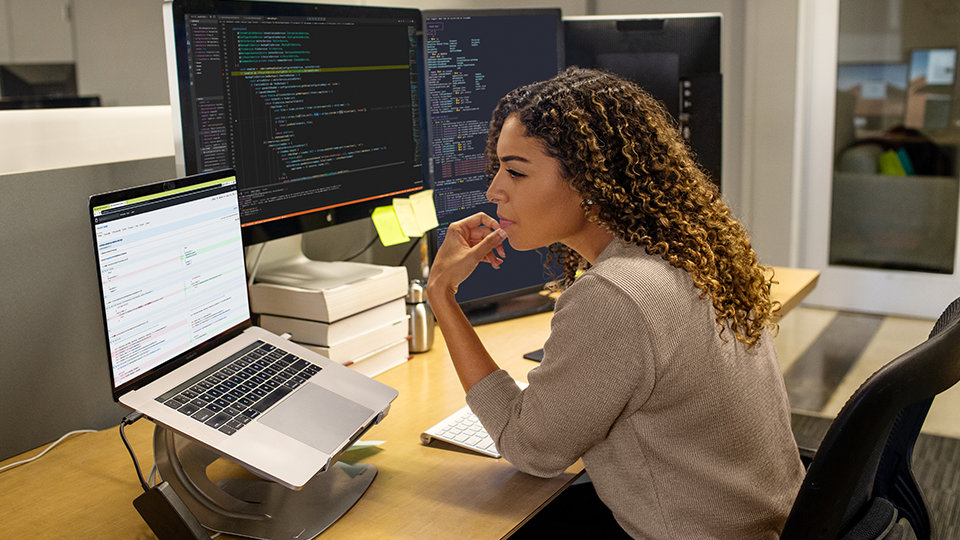 Een ontwikkelaar gebruikt Visual Studio om te coderen op drie beeldschermen op het werk.