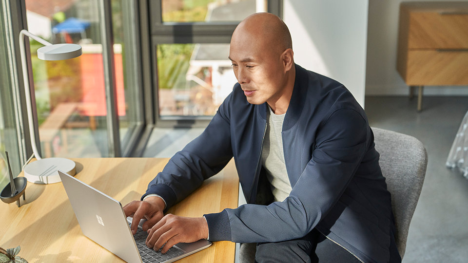 A person seated at a desk uses a Surface Laptop Go 2 for Business. 