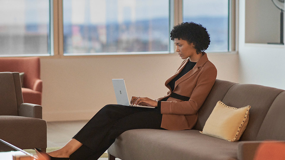 A person sitting on a couch uses a Surface Laptop Go 2 for Business. 