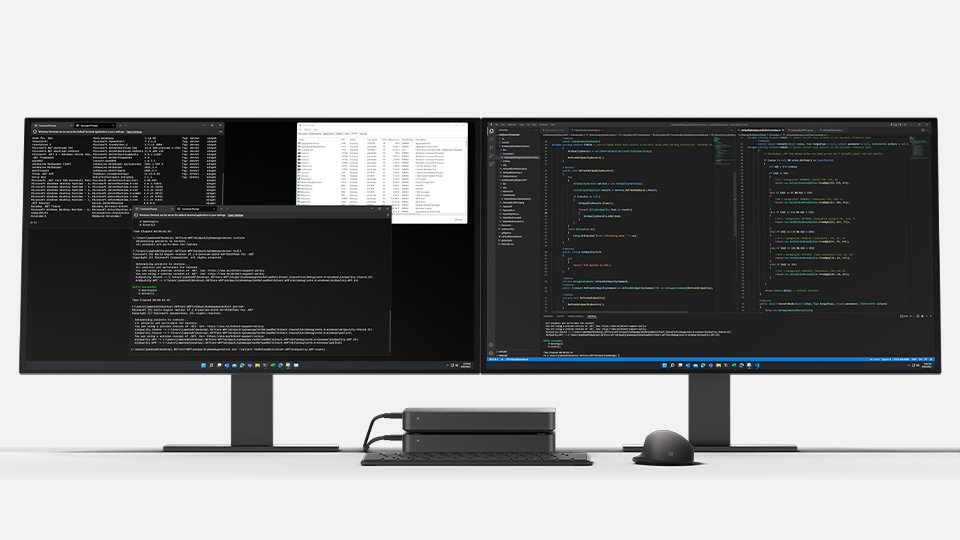 An angled view of a Windows Dev Kit connected to two desktop computer displays that are running developer apps. 